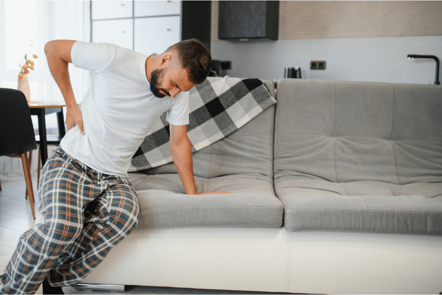 Moški, ki sedi na kavču in se zaradi bolečine drži za ledveno hrbtenico